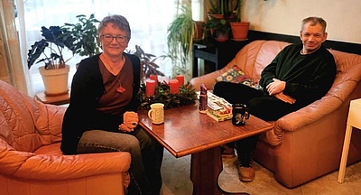 Foto: Martina Knopp und Franz R. sitzen auf zwei Sofas sich gegenüber und lächeln in die Kamera
