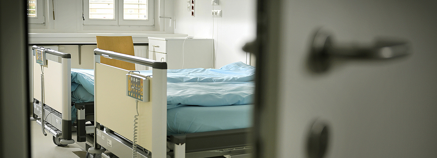 Foto: eine offene Tür zum Patientenzimmer, darin Krankenhausbetten