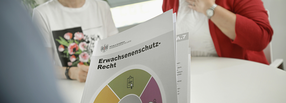 Foto: Erwachsenenschutzrecht-Broschüre, im Hintergrund zwei sitzende Personen