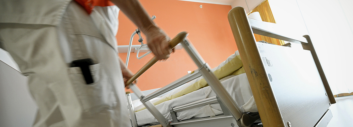 Foto: eine Pflegekraft hantiert an den Seitenteilen eines Pflegebetts