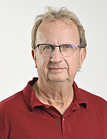 ein Mann mit blond-grauen Haaren und Brille, er trägt ein rotes Poloshirt