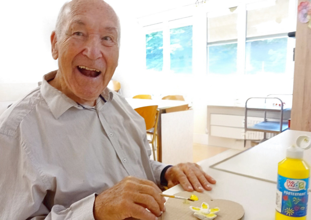 Foto: Älterer Herr lacht in die Kamera. Er hat einen Pinsel in der Hand und bemalt ein Herz.