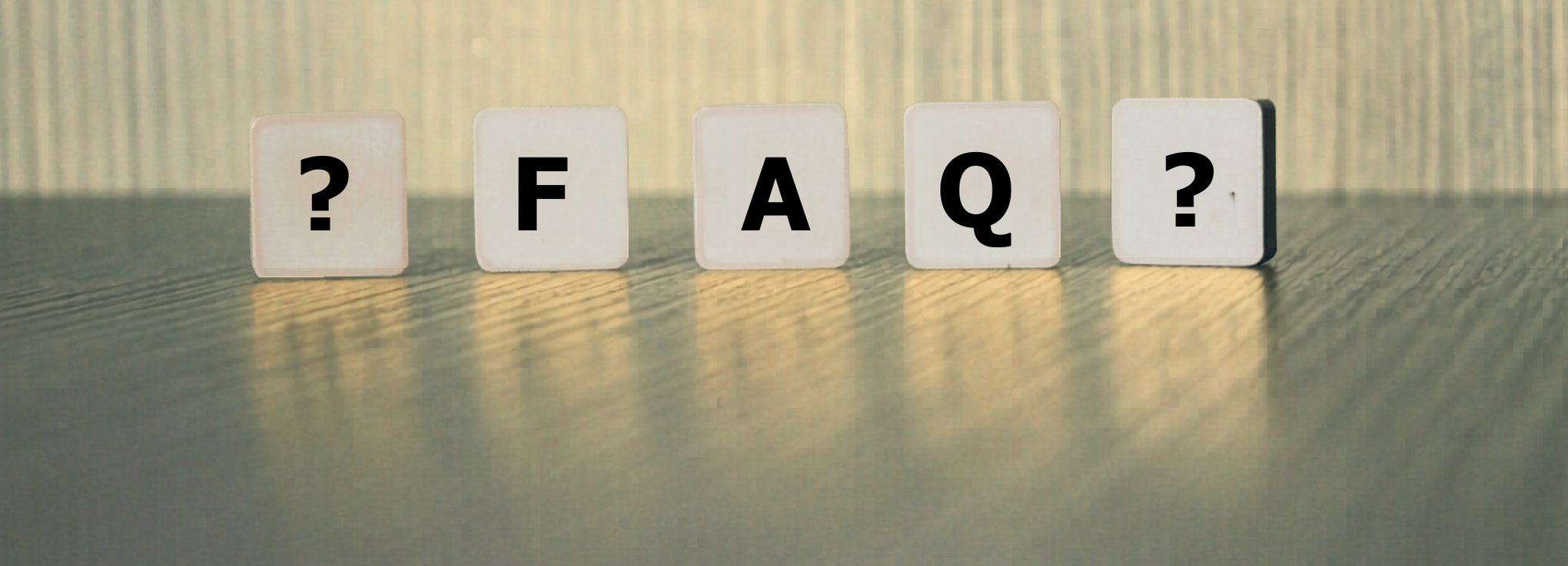 Fünf weiße Würfel auf einem hellen Holztisch vor einem strukturierten Hintergrund; die mittleren drei Würfel zeigen die schwarzen Buchstaben "F", "A", "Q", die äußeren beiden Würfel enthalten jeweils ein großes Fragezeichen – symbolisiert FAQ/Fragen und Antworten.