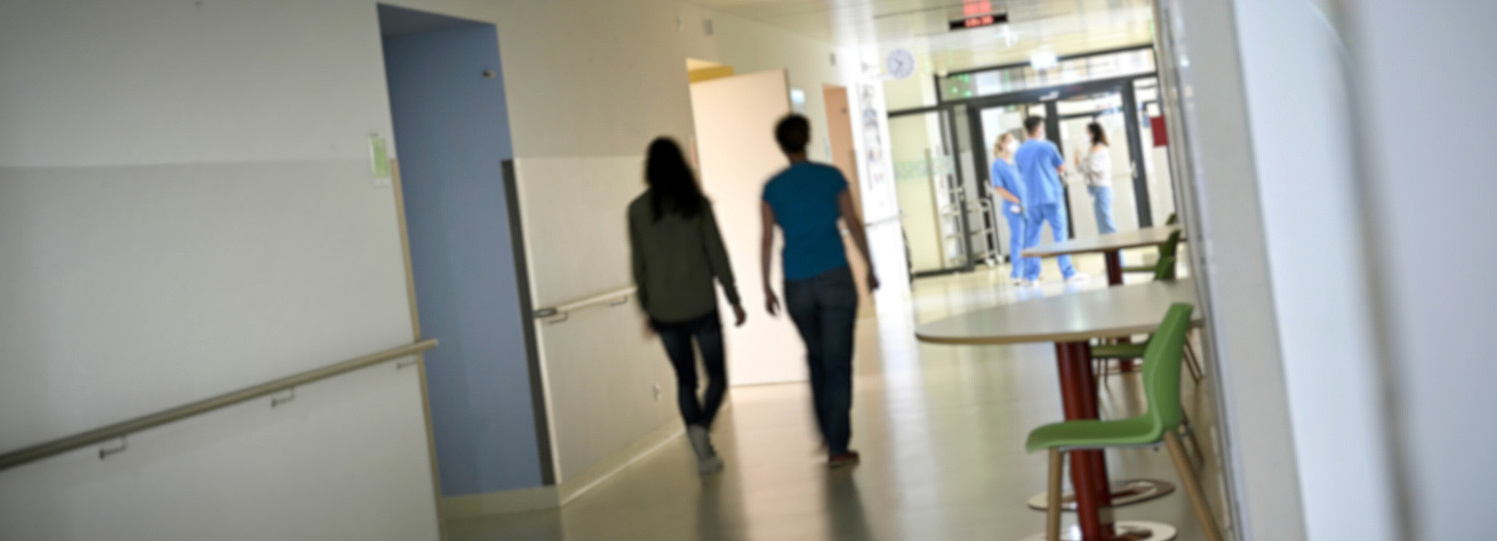 Foto: Krankenhausgang, zwei Frauen in Rückenansicht entfernen sich von der Kamera