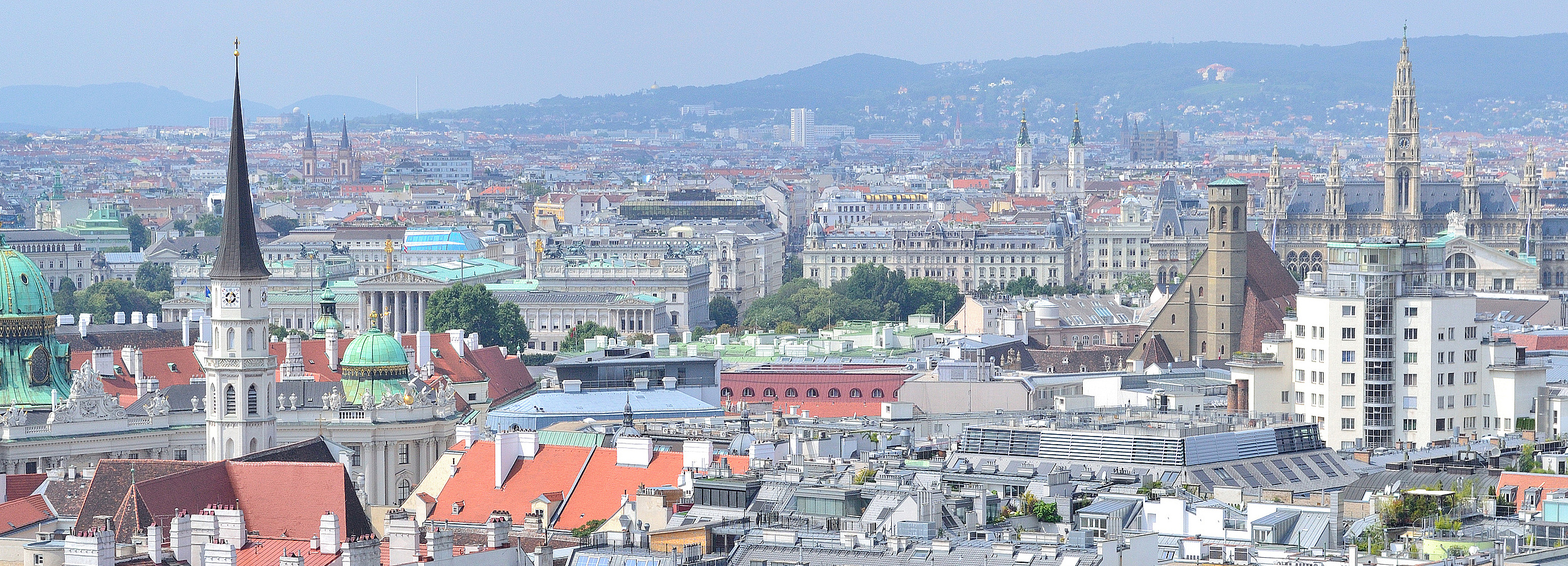 Erwachsenenvertetung in Wien VertretungsNetz FC: iStock Foto von Wien: Panoramablick über die Dächer von Wien mit dicht bebauter Innenstadt, historischen Gebäuden, Kirchtürmen und Kuppeln, modernen Häusern im Hintergrund sowie sanften Hügeln unter einem leicht dunstigen, hellen Himmel.