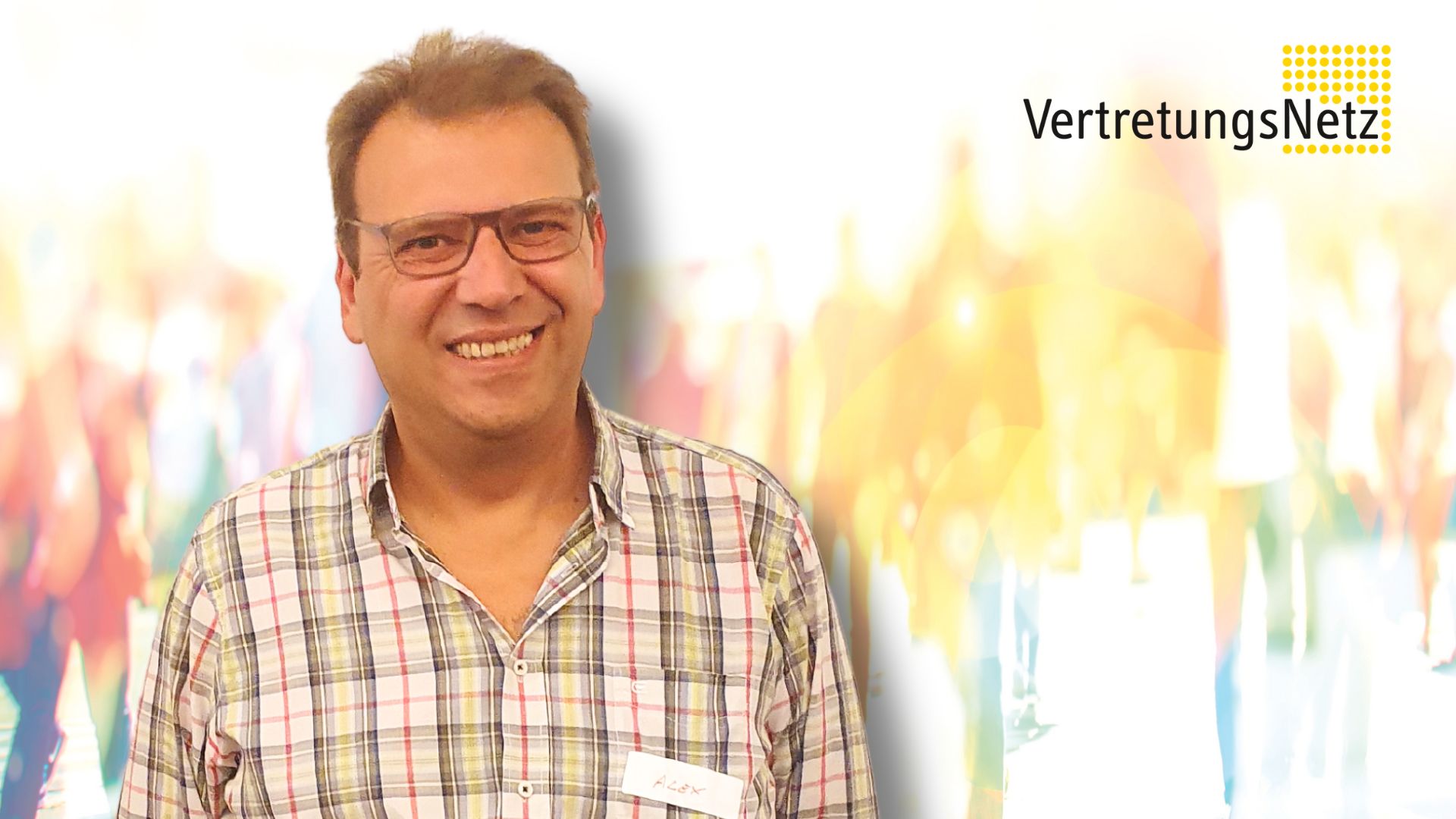 Porträt einer lächelnden Person mit Brille und kariertem Hemd, mit Namensschild, vor hellem unscharfem Hintergrund; oben rechts das Logo „VertretungsNetz“