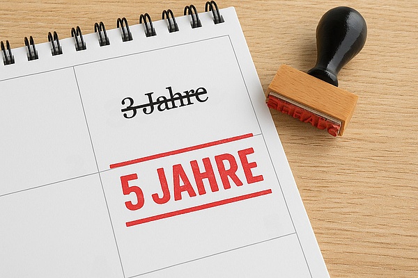 ein Kalenderblatt mit Eintrag: "3 Jahre" in schwarzer Schrift ist durchgestrichen, in roter Farbe steht nun "5 Jahre", neben dem Kalender liegt ein Stempel