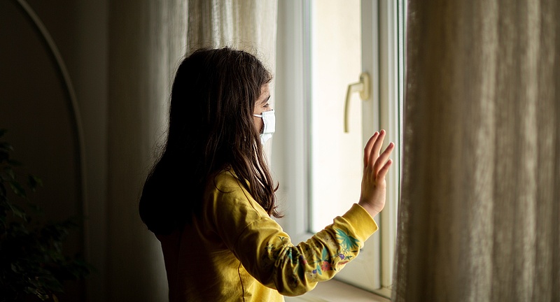 Foto: junges Mädchen in abgedunkeltem Raum, blickt aus dem Fenster