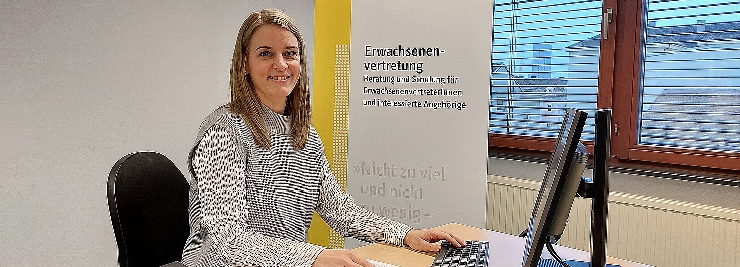 Foto: Sarah Höllriegel sitzt an ihrem Arbeitsplatz, lächelt in die Kamera
