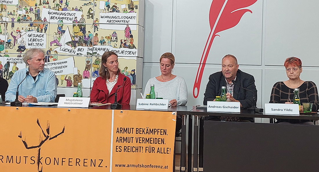 Pressekonferenz der Armutskonferenz, Andreas Gschaider, Martin Schenk, Magdalena Holztrattner, Sabine Rehbichler und Sandra Yildiz. Sie sitzen gemeinsam an einem Tisch, dahinter ein Bild mit Forderungen der Armutskonferenz, vor dem Tisch ein oranges Transparent mit der Aufschrift "Armut bekämpfen, Armut vermeiden. Es reicht! Für alle"