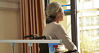 Foto: ältere Frau im Rollstuhl im Pflegeheim, Rückenansicht, sieht aus dem Fenster
