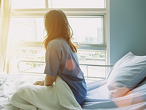 Eine Patientin sitzt auf einem Krankenhausbett und schaut aus dem Fenster ins Licht