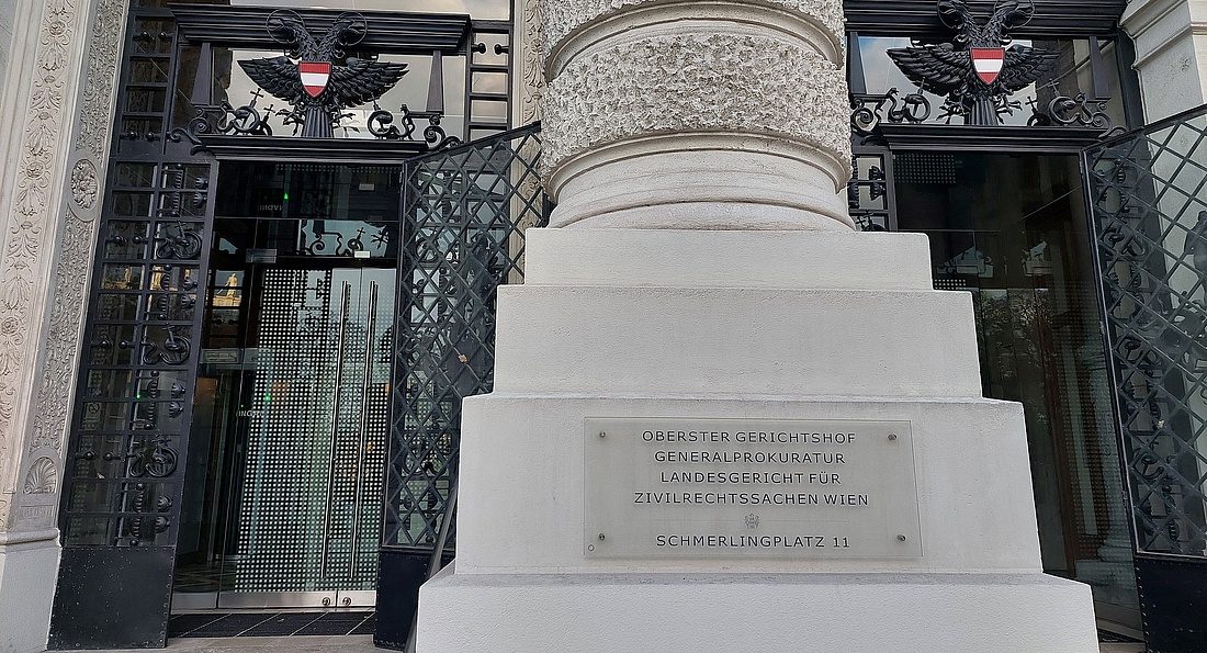 Eingangsbereich des OGH-Gebäudes in Wien, ein schwarzes Tor und eine weiße Säule mit Aufschrift