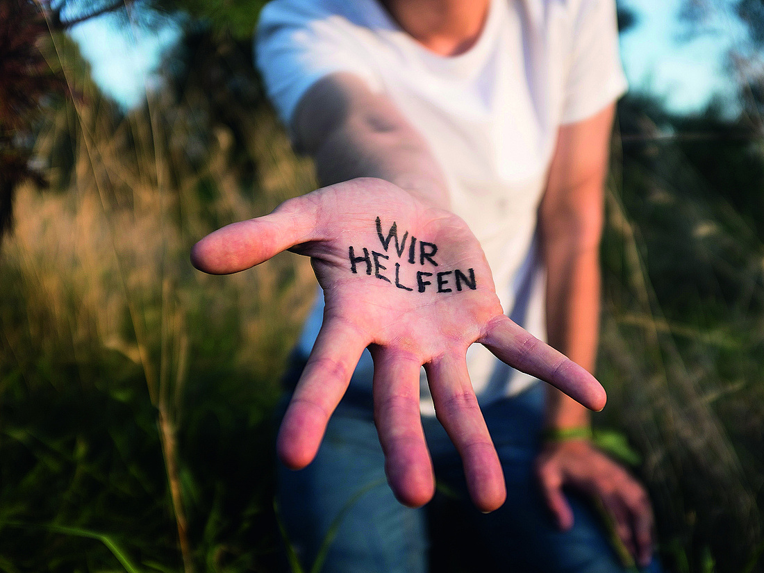 Foto einer ausgetreckten Hand. Darin steht "wir helfen"
