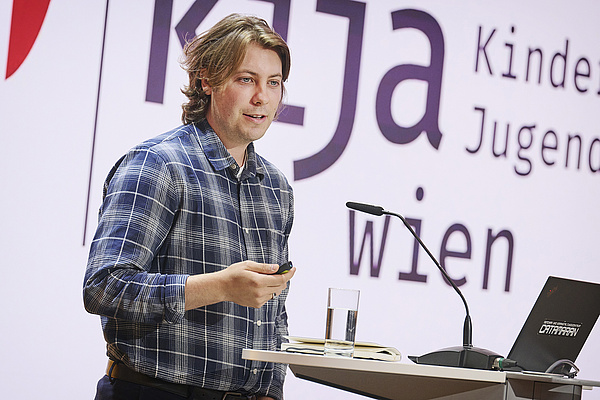 Sebastian Öhner am Stehpult, er trägt kurze brünette Haare und ein kariertes Hemd