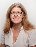 Rita Gänsbacher hat lange brünette Haare und trägt eine Brille sowie eine helle Bluse