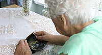 eine alte Frau sitzt an einem Tisch im Pflegeheim und sieht in ihre geöffnete Geldtasche, in der sich lediglich einige Münzen befinden