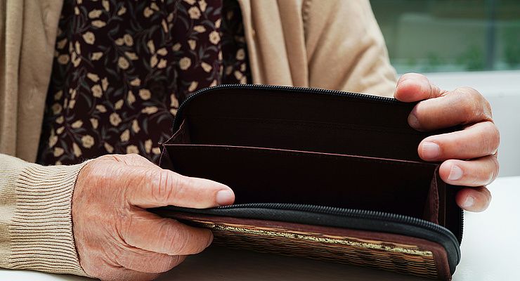 eine alte Frau öffnet eine leere Geldbörse, man sieht ihren Oberkörper und Hände