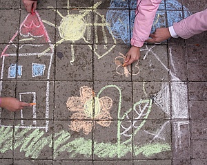 Foto: Kinderhände zeichnen ein Haus und Blumen auf die Straße