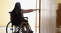 Frau im Rollstuhl versucht eine Tür im Pflegeheim zu öffnen