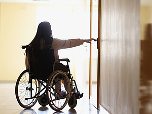 Frau im Rollstuhl versucht eine Tür im Pflegeheim zu öffnen