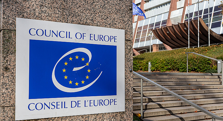Stufen zum Gebäude des Europarats, links davon das blaue Logo des Europarats auf einem Schild an einer Mauer